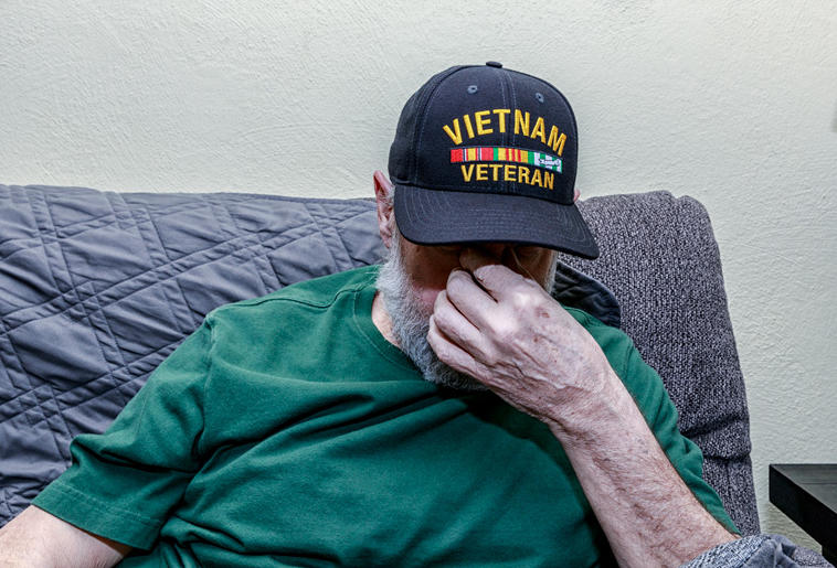 A depressed Vietnam War USA military veteran has his head down while covering his face with his hand