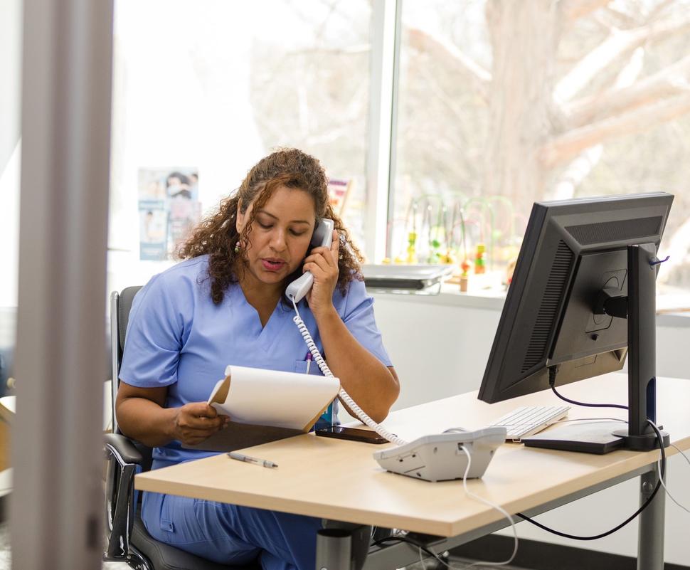 Una mujer con uniforme azul en un consultorio habla por teléfono.