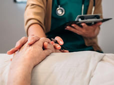  Una enfermera toca las manos de un paciente mayor acostado en una cama de hospital.