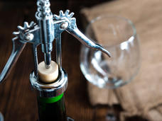 A bottle of wine being opened with a metal opener.