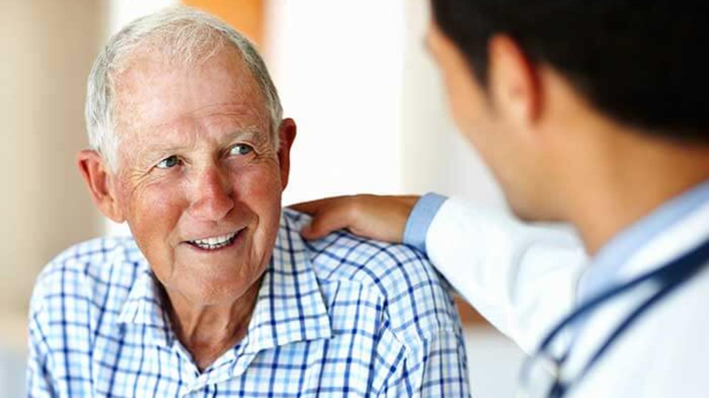 Man with white hair smiles at a male doctor who faces him and has a hand on the man's shoulder.