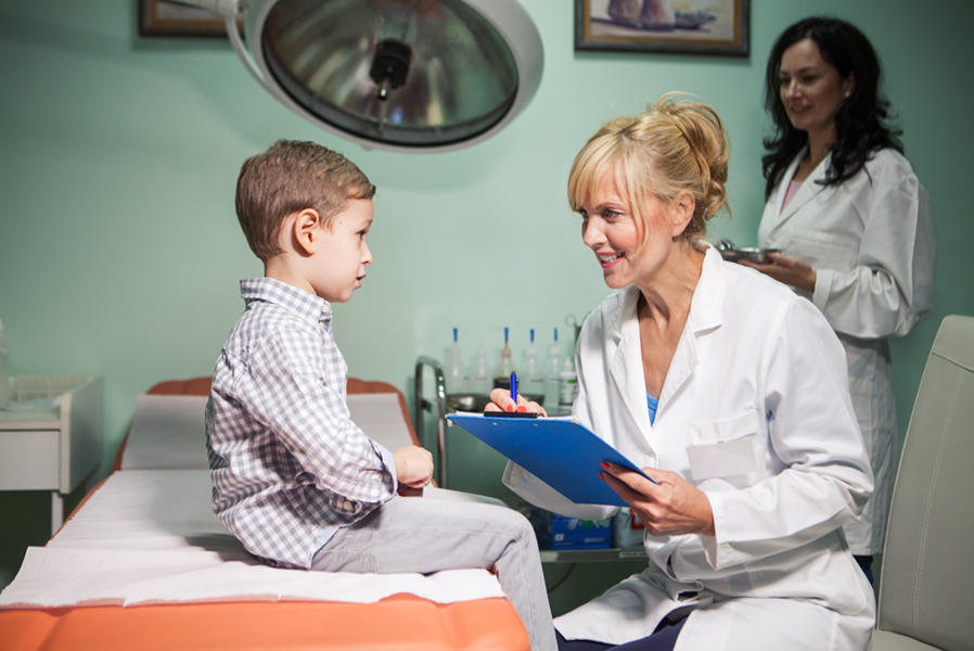 A doctor talks to a small boy who sits on a hospital bed