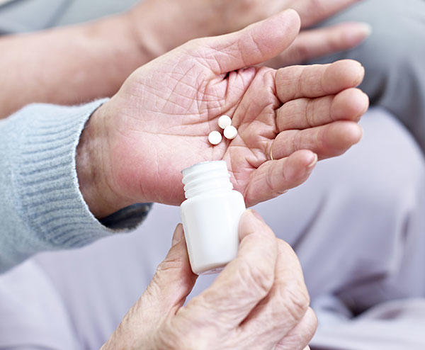 Person with cancer putting pill in her hand, as she gets ready to take the medicine.  