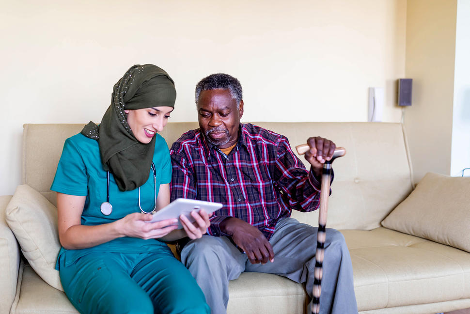 Healthcare worker in headscarf shows older Black male information on a tablet