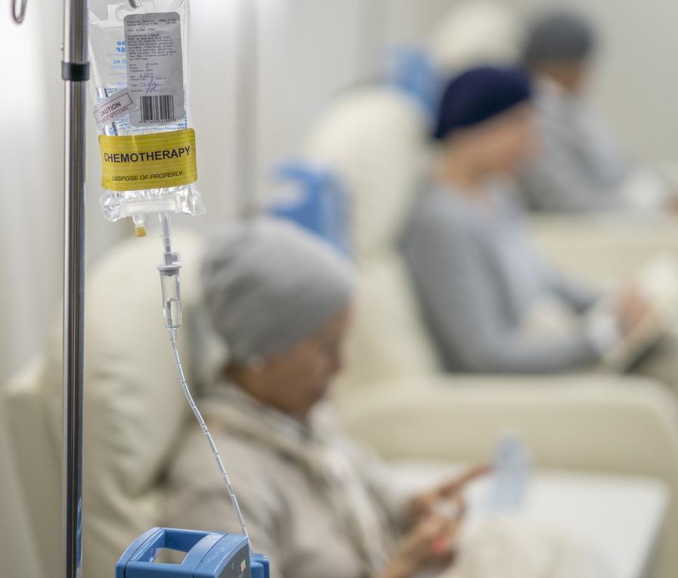 A chemotherapy bag hanging and a woman receiving treatment sitting in a chair.