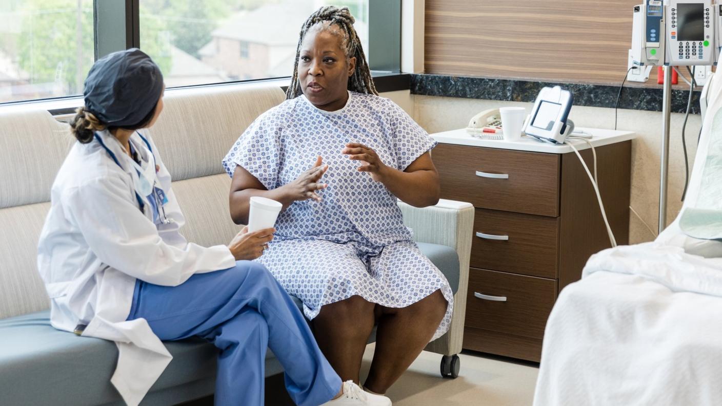 Foto de una mujer de mediana edad en la habitación del hospital conversando con una cirujana.